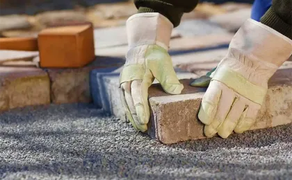 Handwerker mit Schutzhandschuhen setzt Pflastersteine präzise ins Splittbett. Fachgerechte Pflasterarbeiten im Garten.