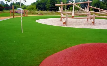 Robuster Kunstrasen auf einem öffentlichen Spielplatz mit Holz-Klettergerüst. Sicherer künstlicher Rasen für Kinder.