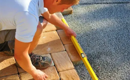 Ein Landschaftsgärtner prüft das frisch verlegte Pflaster mit einer gelben Wasserwaage auf exakte Ausrichtung.