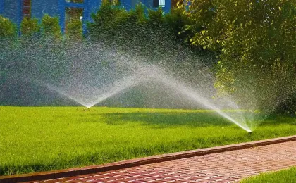 Zwei Versenkregner bewässern gleichzeitig eine große Rasenfläche neben einem Pflasterweg. Moderne Gartenbewässerung.
