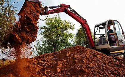 Ein roter Kettenbagger schüttet einen großen Haufen braune Erde auf. Kraftvolle Baggerarbeiten bei den Erdarbeiten.