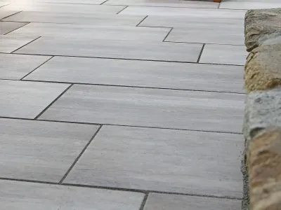 Moderne Platten auf einer Terrasse, sauber verfugt und flankiert von einer Mauer aus Naturstein.