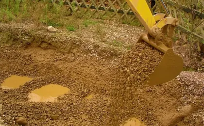 Ein gelber Bagger löffelt steinige Erde bei Erdarbeiten im Garten. Professionelle Baggerarbeiten für Fundamente.