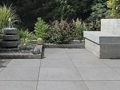 Elegante Terrasse aus Naturstein mit einem plätschernden Brunnen und einer massiven Steinbank.