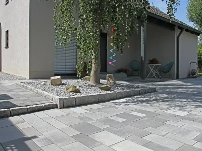 Großflächige Pflasterarbeiten für eine moderne Einfahrt mit integriertem Baumbeet und Graniteinfassung.