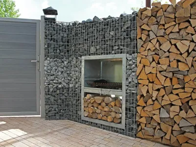Ein langlebiger Garten-Grill verbaut in einer Gabionenwand aus Naturstein direkt neben einem modernen Zaun.